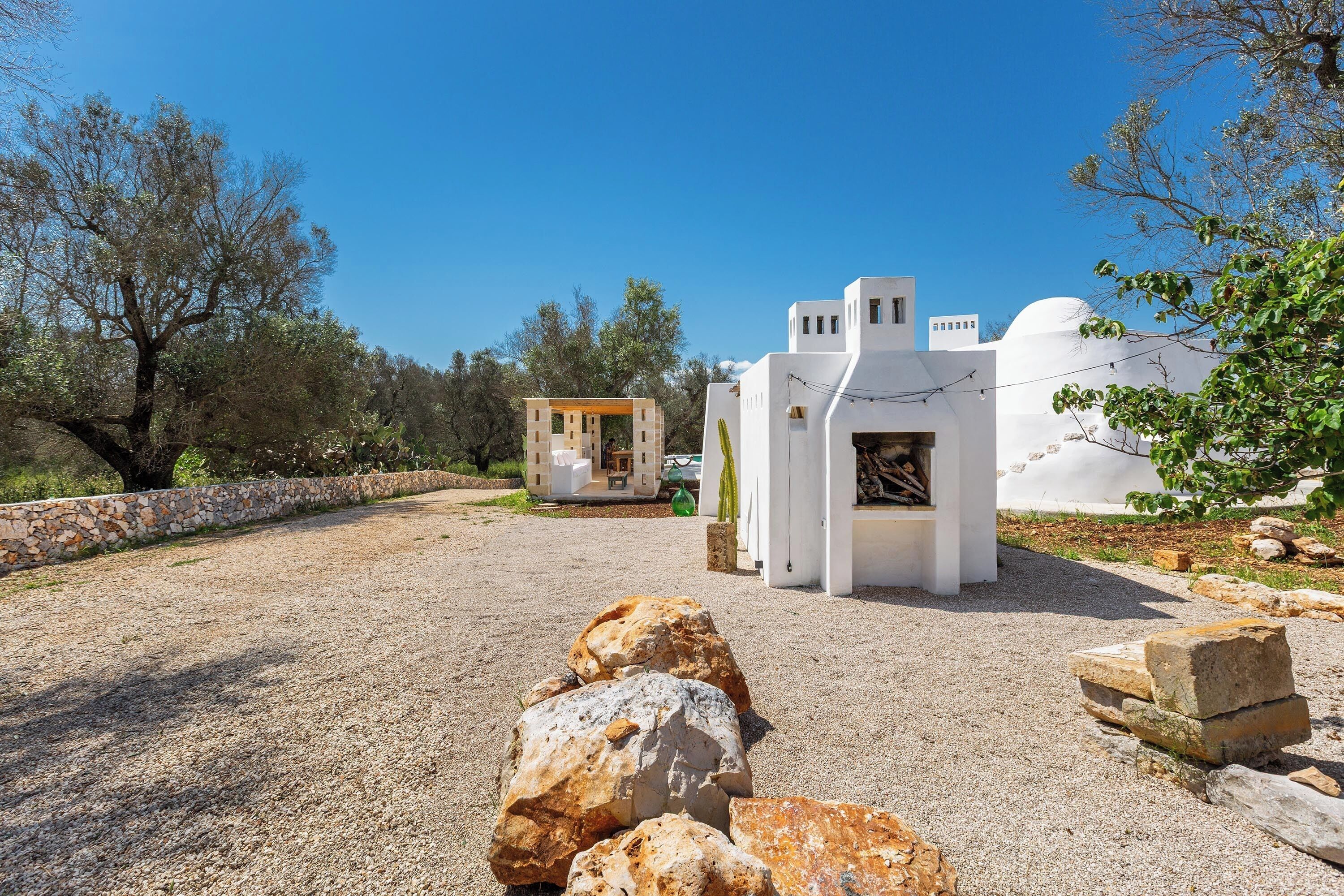 A white building with a dome and a small structure with a door, surrounded by rocks and trees.