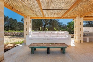 Ein Sitzbereich im Freien mit einer weißen Couch und einem Holztisch, unter einer Holzpergola.