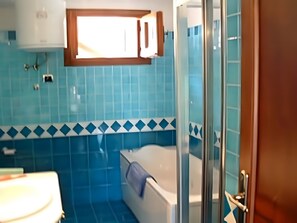 Un baño con azulejos azules, una bañera, una ducha y un ventanal.