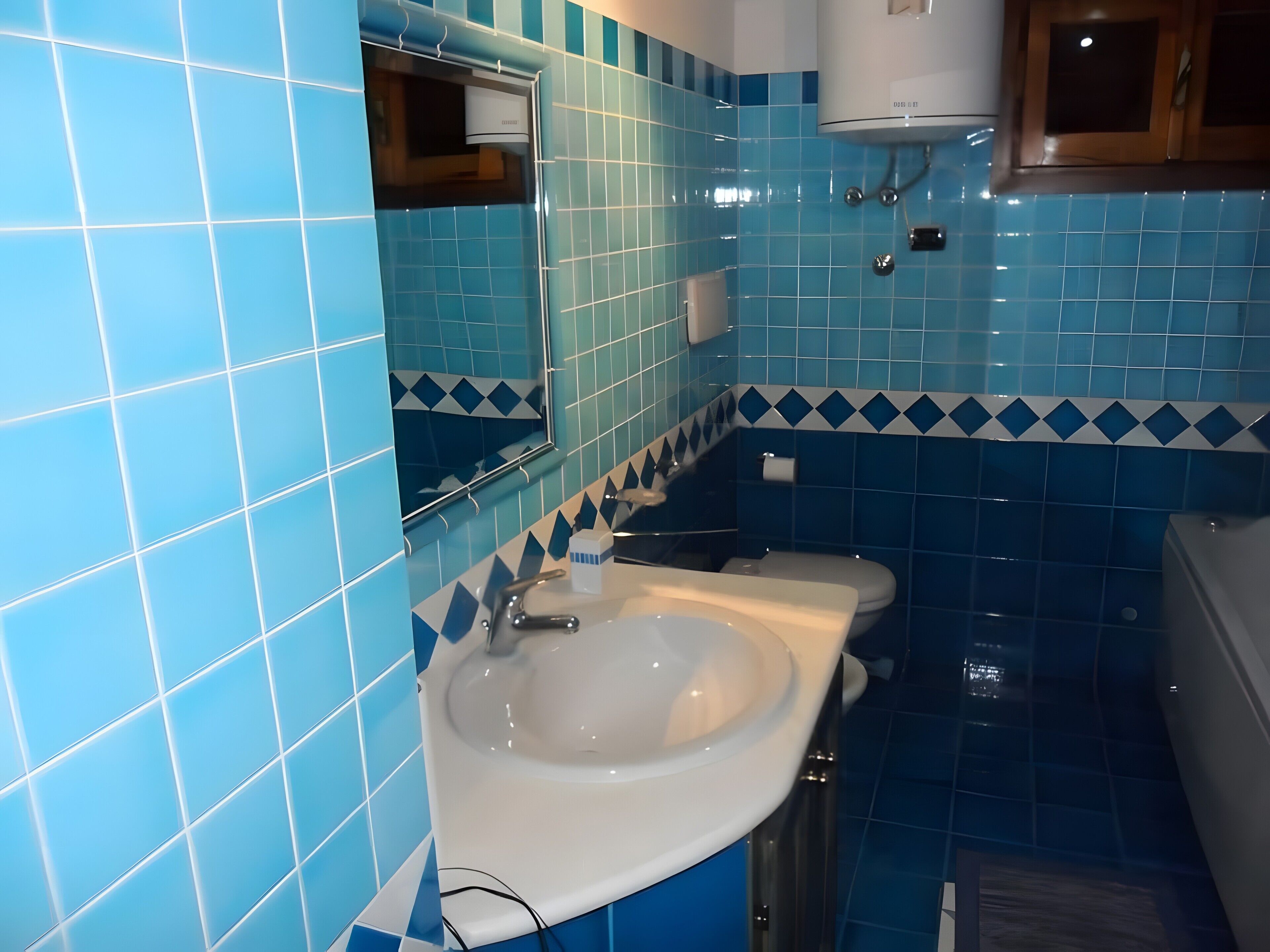 A bathroom with blue tiles, a white sink, and a mirror.