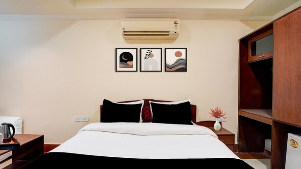 Quarto de hotel com uma cama, mesa de cabeceira, cafeteira, ar condicionado fixado na parede e três obras de arte emolduradas.
