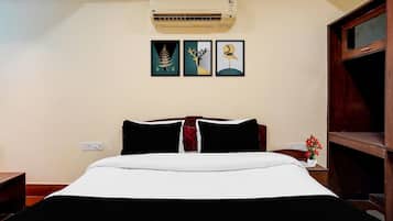 A hotel room with a bed, an air conditioner, and three framed artworks on the wall.