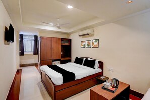 A hotel room with a bed, a bedside table with a kettle, a wardrobe, and a ceiling fan. - Classic Banshi Bhawan (Prayagraj)