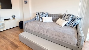 Une chambre moderne avec un canapé-lit gris, un téléviseur à écran plat et une petite table de chevet.