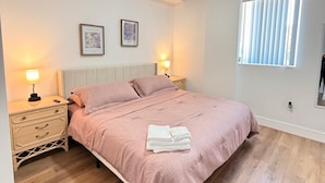 Une chambre à coucher comprenant un lit, des tables de chevet, une fenêtre et des œuvres d’art accrochées au mur.