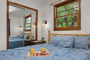 Una camera da letto con un grande specchio, una testiera in legno, una finestra vista alberi e un vassoio per la colazione sul letto.