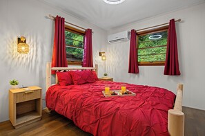 Una camera da letto con copriletto rosso, una testiera in legno, due comodini, un tavolino e un vassoio per la colazione, oltre a una finestra con tende.