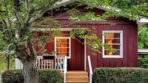 A red wooden house with a porch, a window, and a tree in front. - Bryson City Cabin · Sleeps 5 · Pets OK · Fire Pit (Whittier)