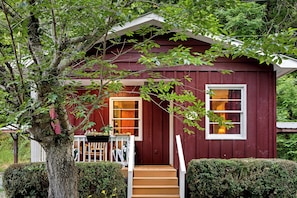 Una casa di legno rossa con un portico, una finestra e un albero di fronte.