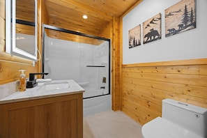 Un bagno con rivestimenti in legno, cabina doccia in vetro, lavabo con piano in marmo e water.