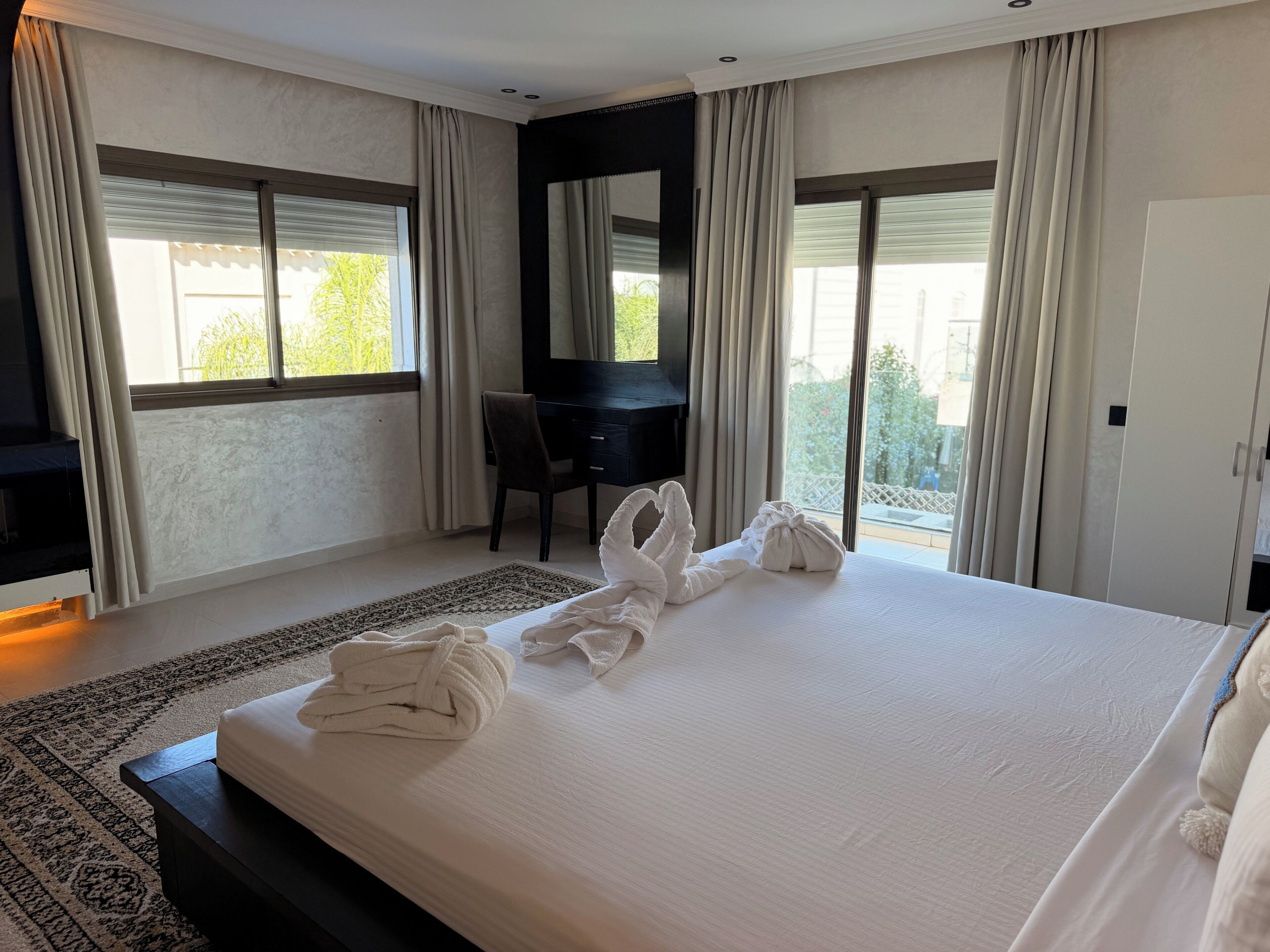 A hotel room with a large bed, a desk, and a view of greenery outside.