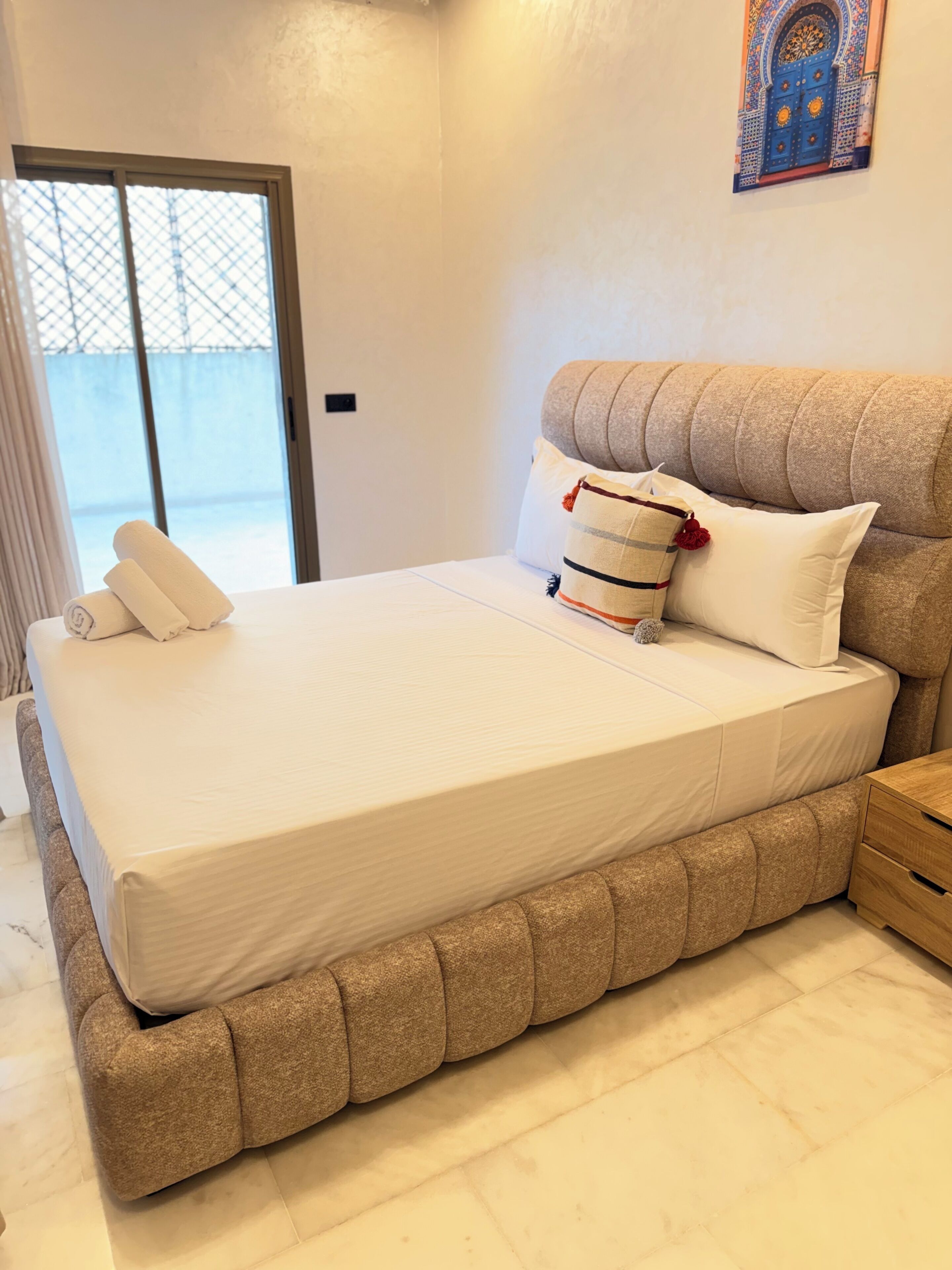 A bedroom with a large bed, a wooden nightstand, and a decorative wall piece.