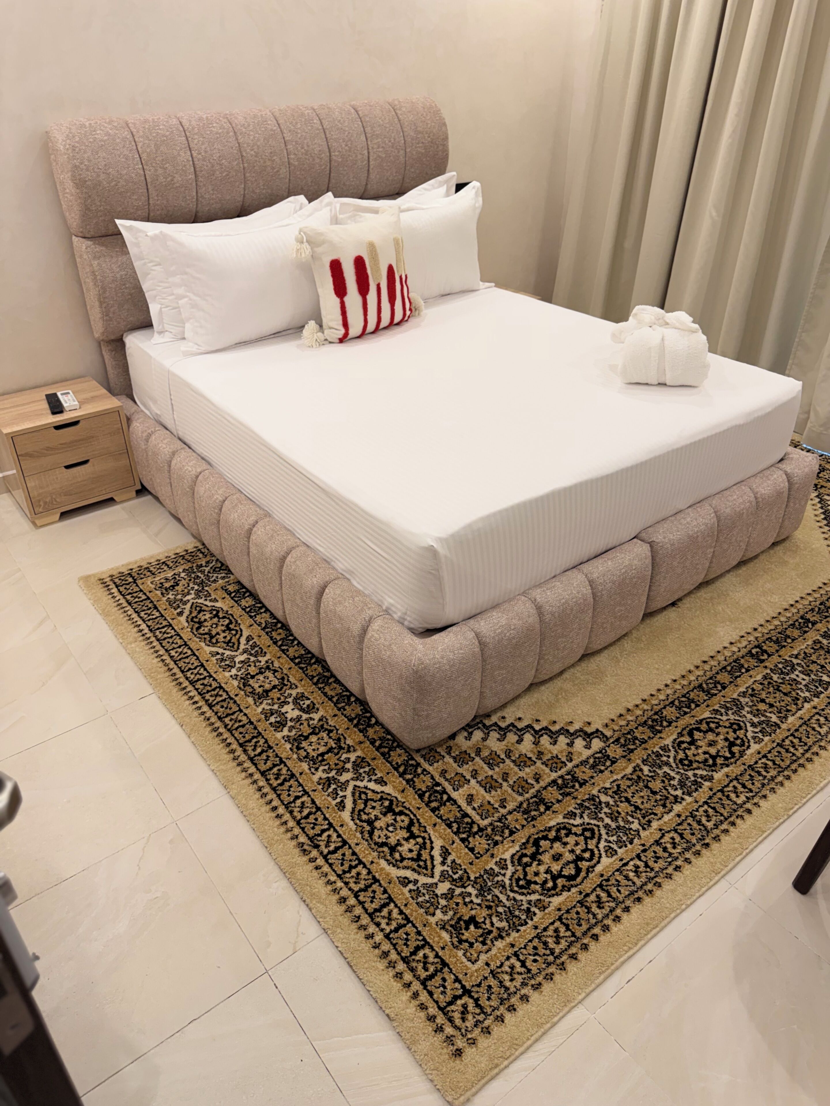 A neatly made bed with a white mattress, a beige headboard, and a patterned rug.