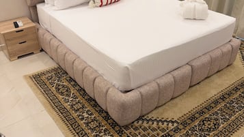 A neatly made bed with a white mattress, a beige headboard, and a patterned rug.