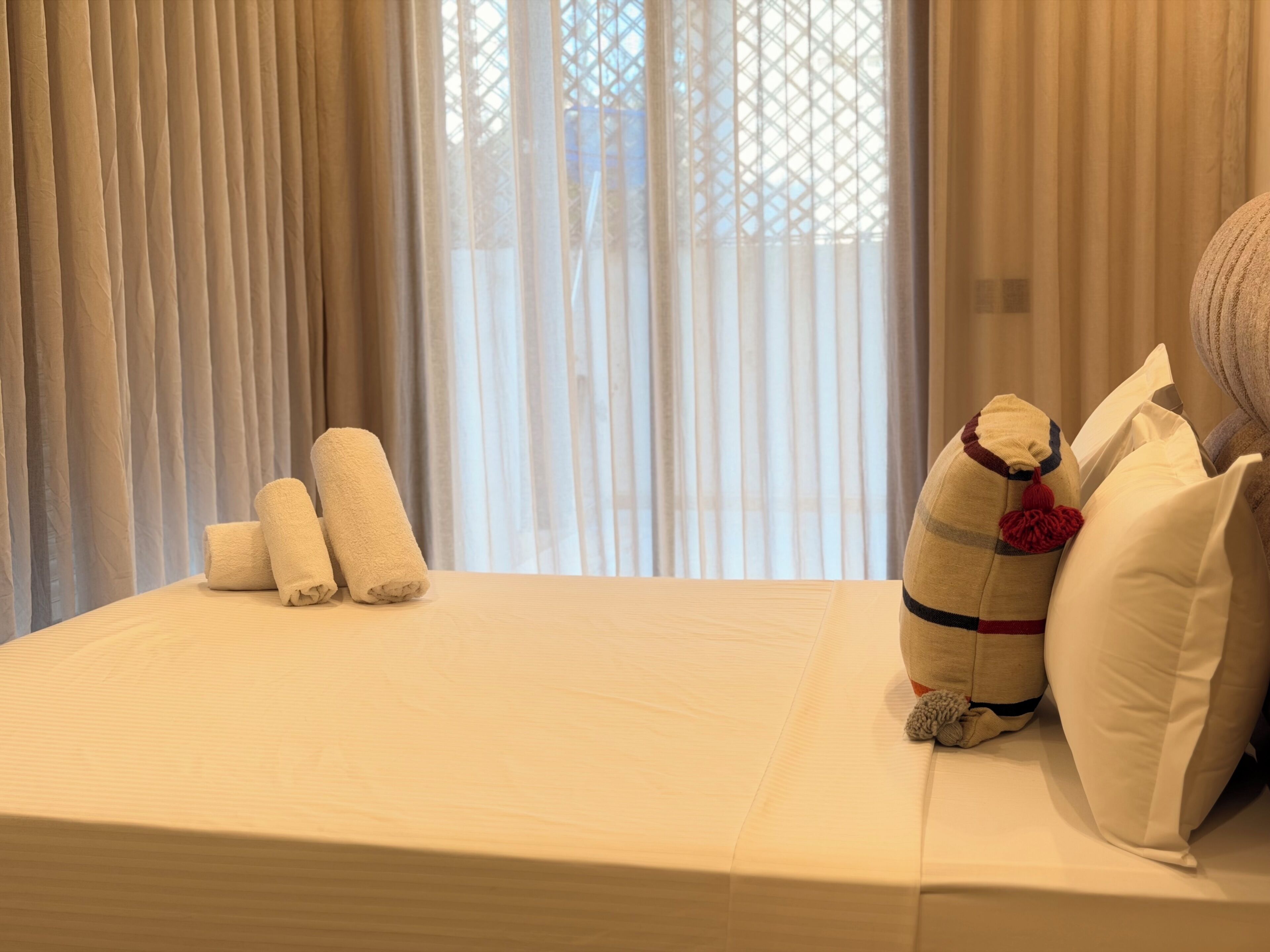 Ett hotellrum med en säng, kuddar och ett fönster med gardiner.