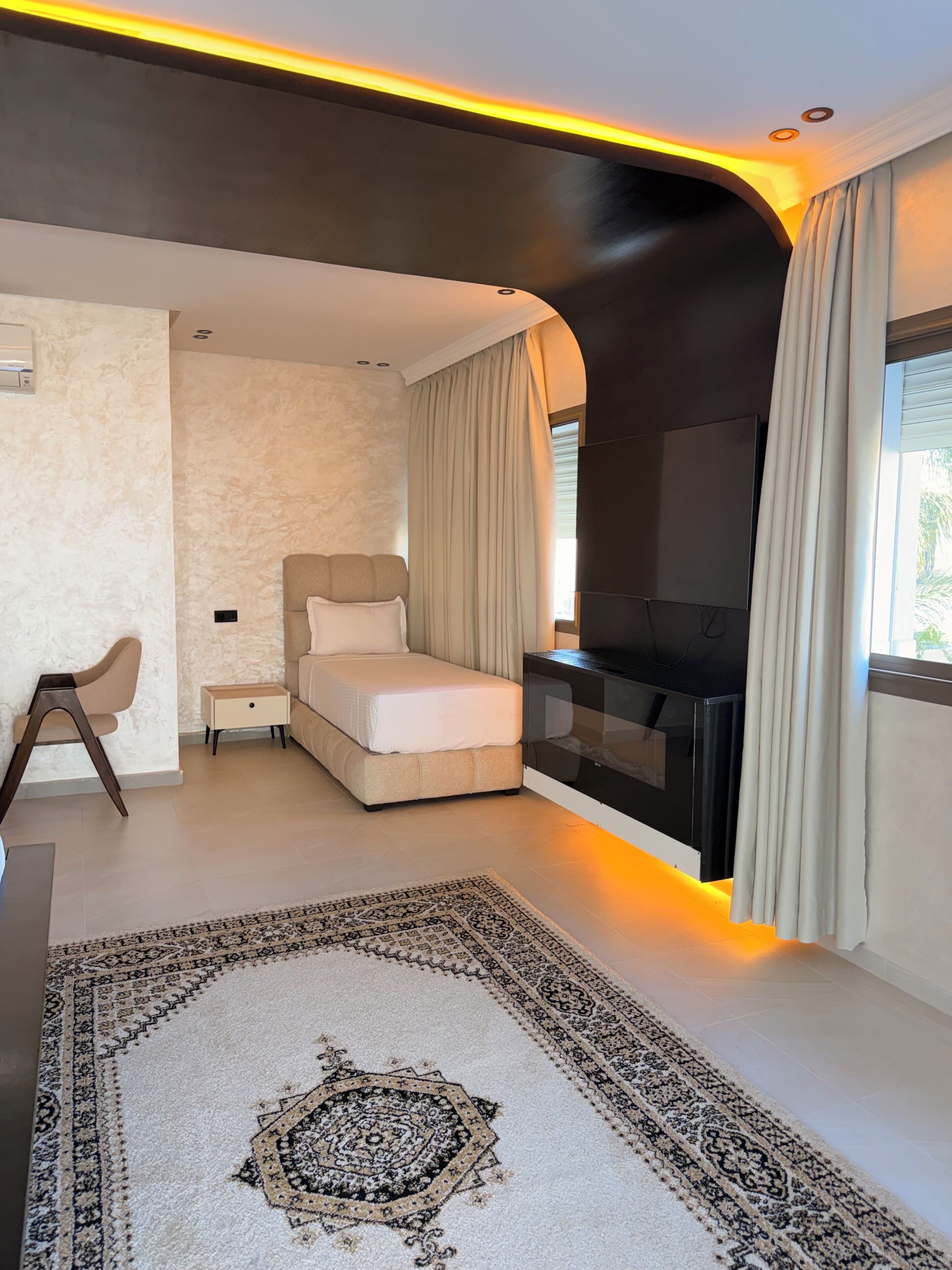 A modern bedroom with a bed, a TV, a small table, and a patterned rug.