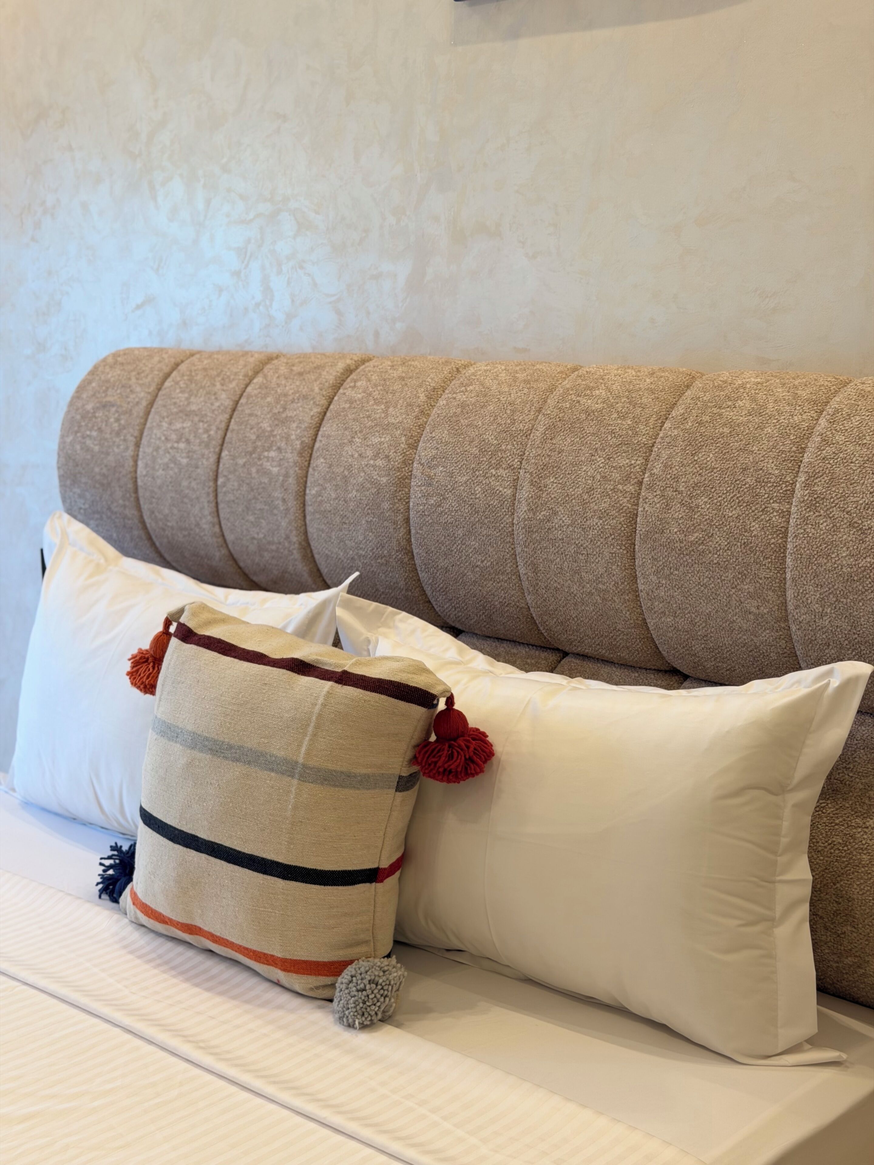 A sofa with multiple cushions, a striped pillow, and a pom-pom.