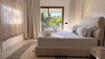 Un dormitorio con una cama grande, una mesita de noche, un tapete estampado y vistas al verdor exterior.