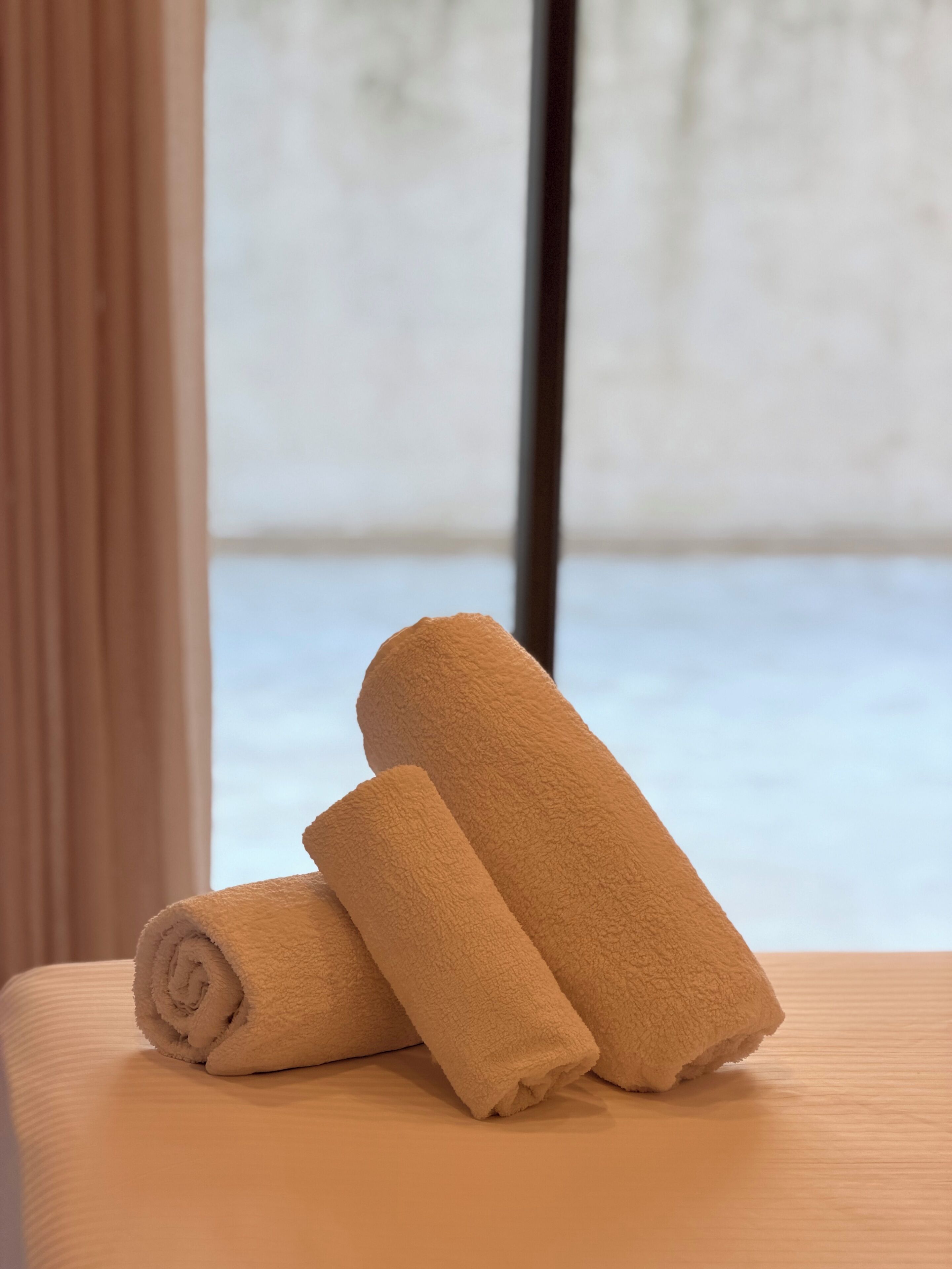 A set of rolled towels on a bed with a view of a snowy landscape through a window.