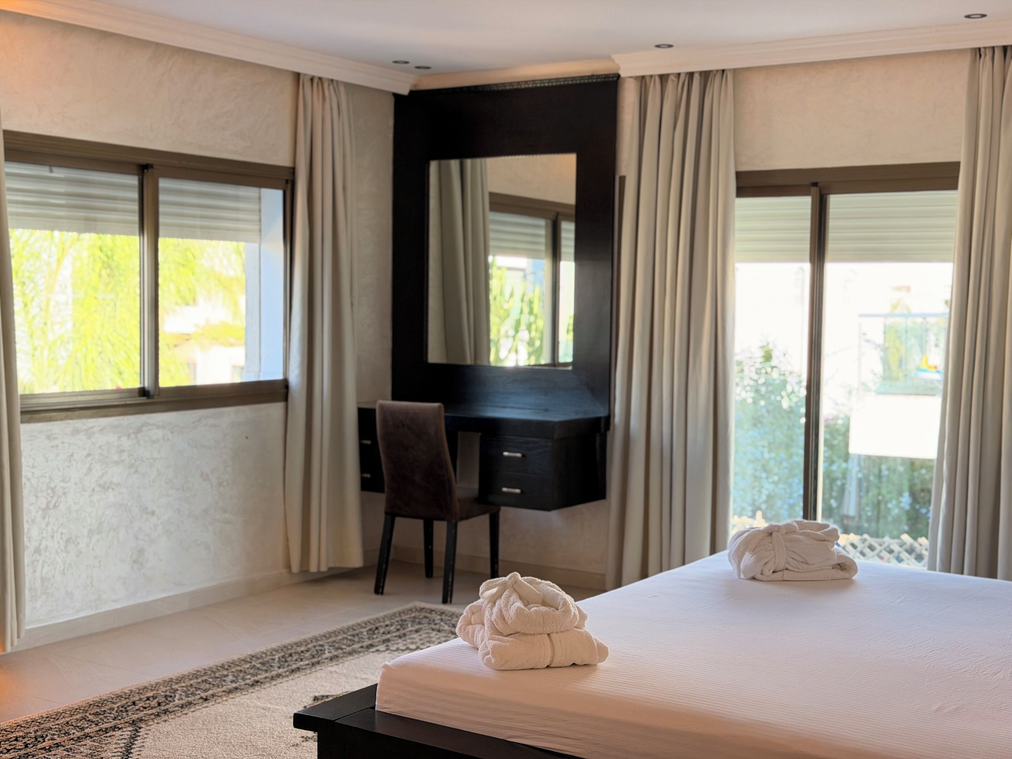 A hotel room with a bed, a desk, a chair, and a large window with curtains.