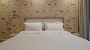 Una cama bien hecha con sábanas blancas, cabecera de madera y un papel pintado con motivos de bicicleta.