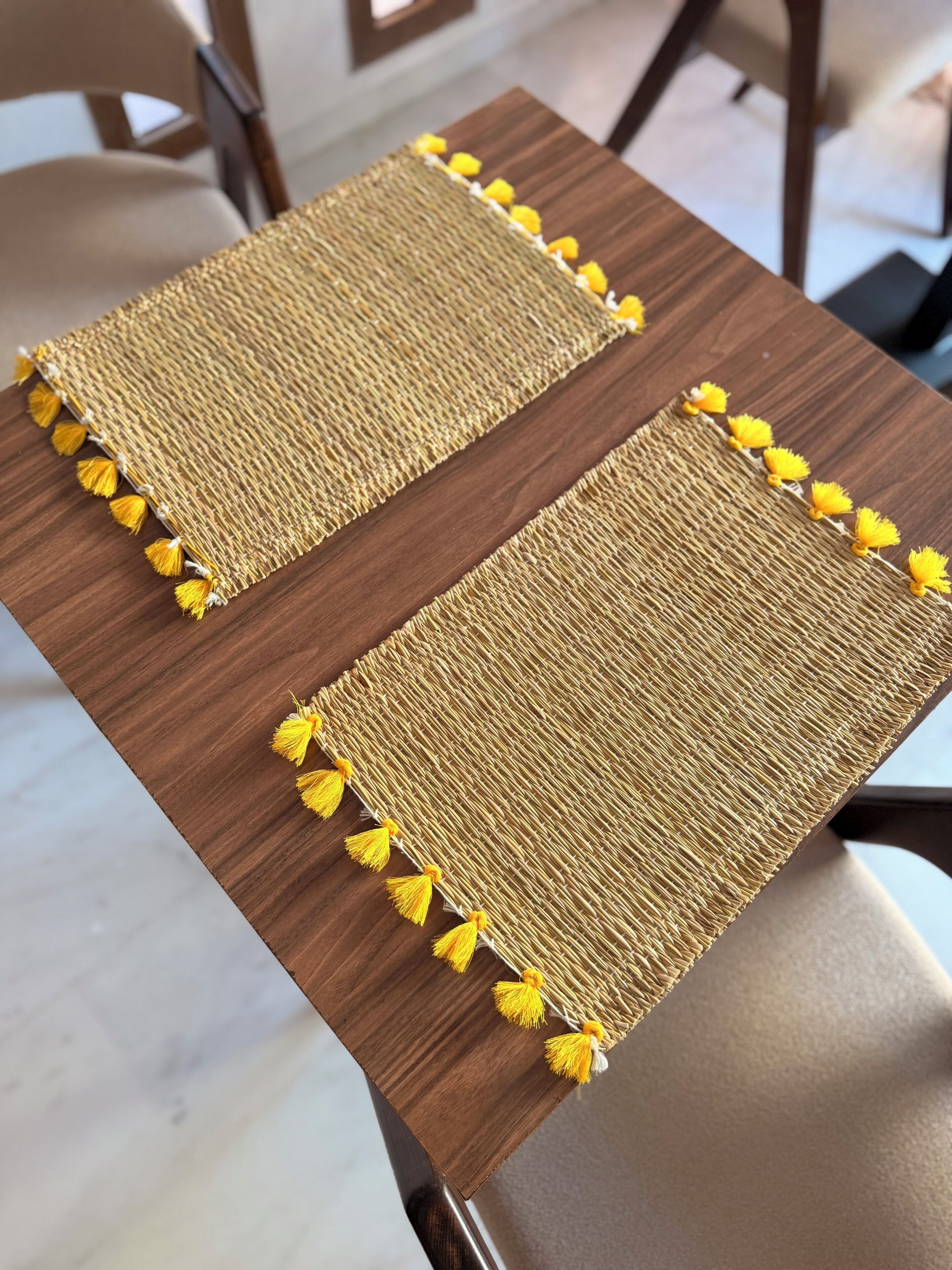 Two woven placemats with tassels on a wooden table.