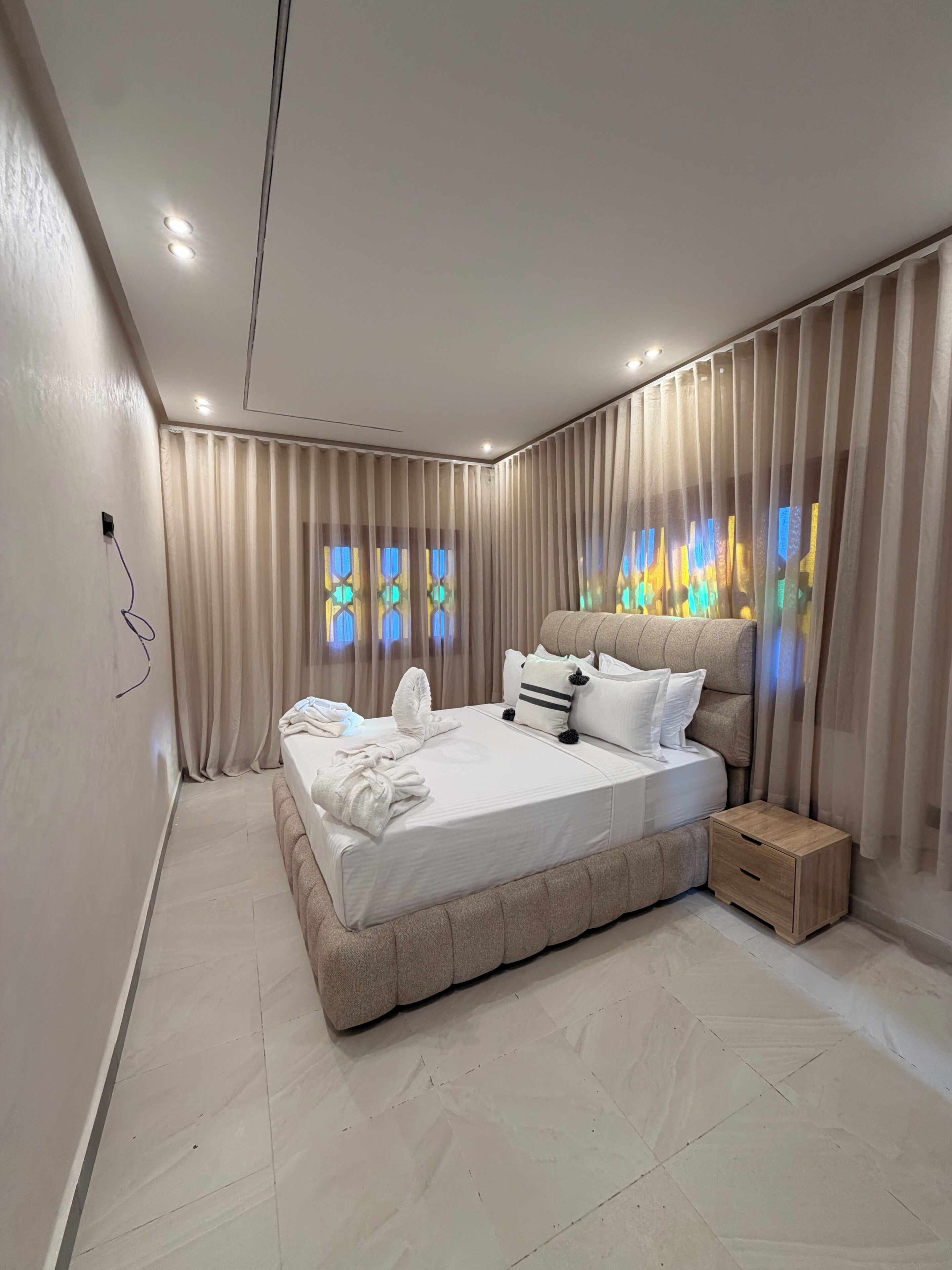A modern bedroom with a large bed, a nightstand, and a wall-mounted power outlet.