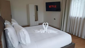 A hotel room with a neatly made bed, a wardrobe, a television displaying 'NETFLIX,' and a window with curtains. - Riad Elizabeth (Nouaceur)