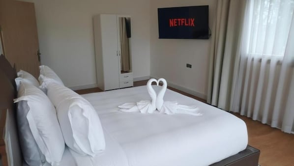 Una habitación de hotel con una cama bien hecha, un armario, un televisor mostrando 'NETFLIX' y una ventana con cortinas.