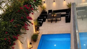 An outdoor swimming pool with a tiled deck, surrounded by potted plants and outdoor furniture. - Riad Elizabeth (Nouaceur)