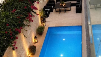 An outdoor swimming pool with a tiled deck, surrounded by potted plants and outdoor furniture.