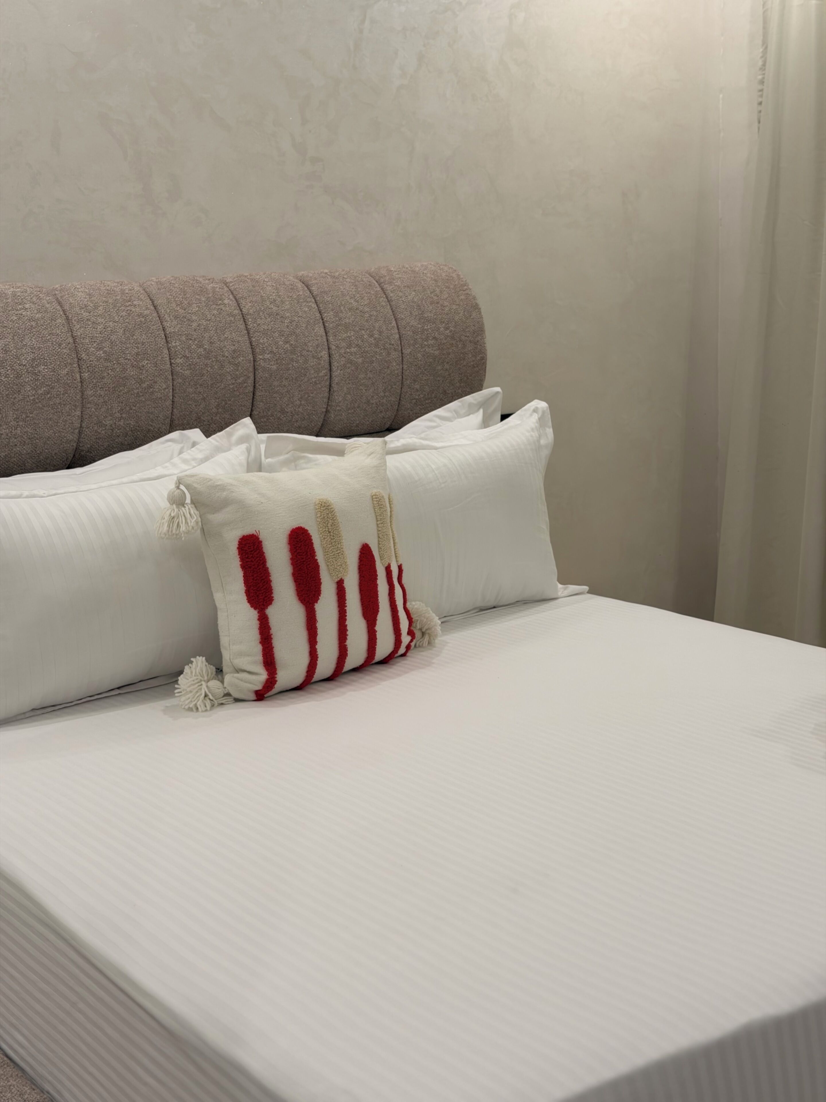 A neatly made bed with white bedding and a single decorative pillow with red stripes.