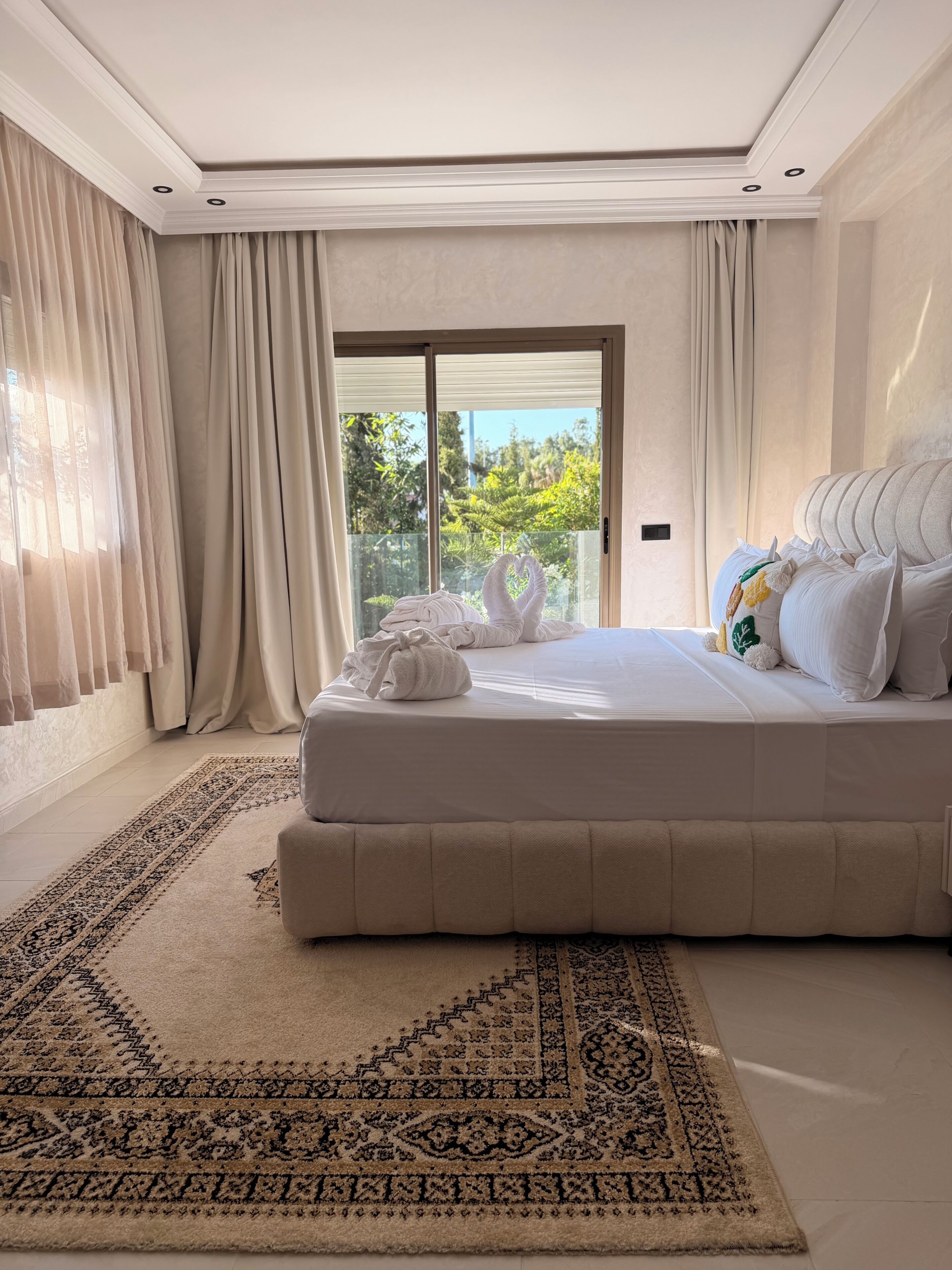 A spacious bedroom with a large bed, a patterned rug, and a view through a sliding glass door.