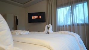 A hotel room with a bed, a wall-mounted television displaying 'NETFLIX,' and a window with curtains. - Riad Elizabeth (Nouaceur)