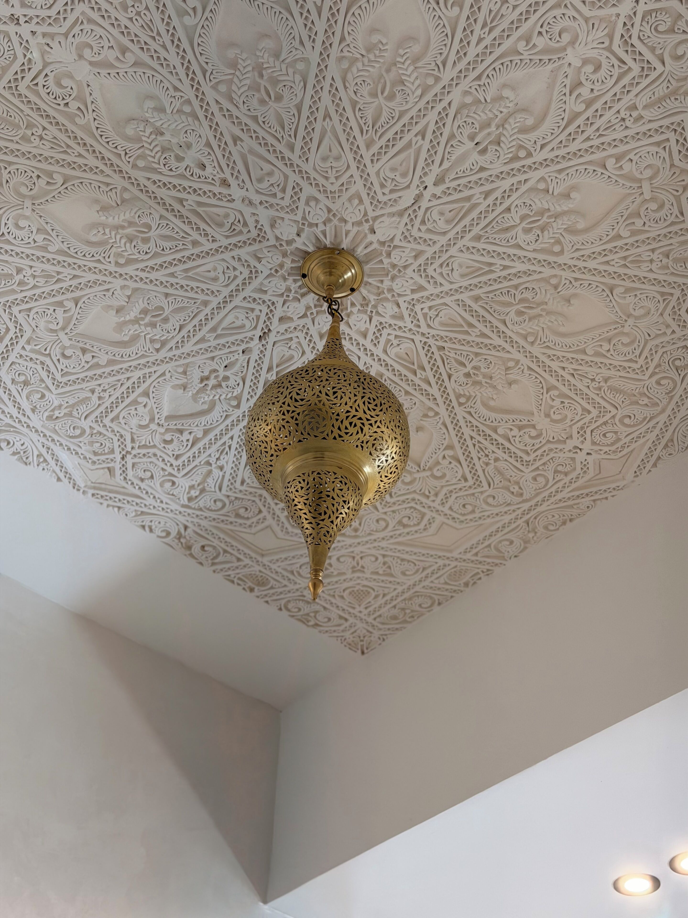 A ceiling with intricate geometric and floral patterns, a hanging brass lantern, and a recessed light fixture.