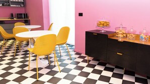 Ein Zimmer mit Schachbrettboden, gelben Stühlen, einem weißen Tisch, einer schwarzen Schubladenschrank und einer rosa Wand.