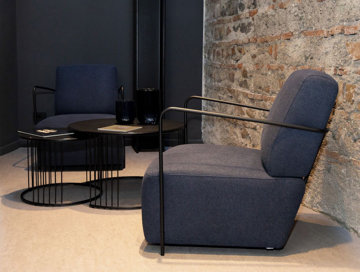 A modern room with a blue armchair, a round black table, and a dark blue sofa.