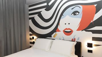 Habitación de hotel con una cama grande, dos mesitas de noche con lámparas, un mural en la pared y una cortina gris.