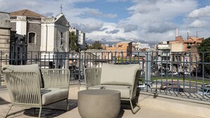 Eine Terrasse mit Korbstühlen und einem runden Tisch, mit Blick auf eine Stadtlandschaft mit Gebäuden und einer Kirche.