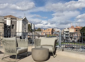 A terrace with wicker chairs and a round table, overlooking a cityscape with buildings and a church. - Made To Measure Catania Centro (Catania)