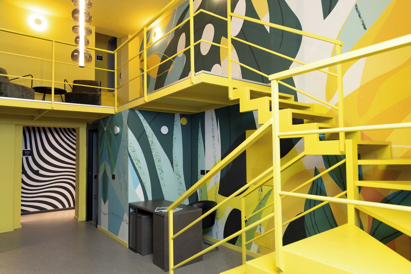 Ein mehrgeschossiges Interieur mit gelben Geländern, abstrakter Wandkunst und einer Treppe.