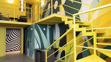 Ein mehrgeschossiges Interieur mit gelben Geländern, abstrakter Wandkunst und einer Treppe.