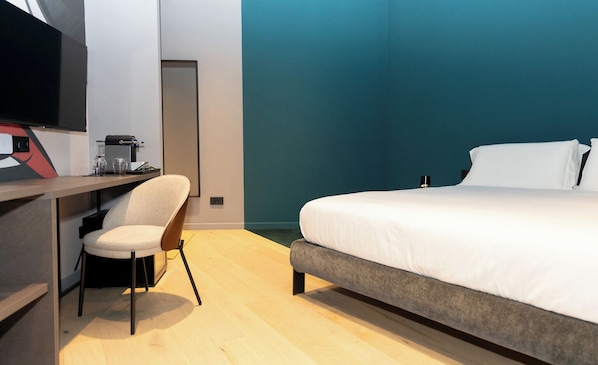 A modern hotel room with a bed, a desk with a chair, a television, and a blue accent wall. - Made To Measure Catania Centro (Catania)