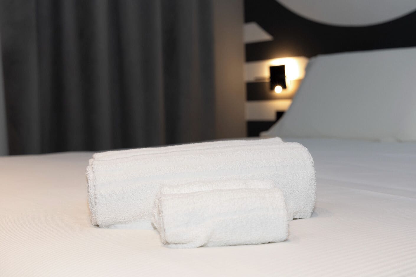 Una cama bien hecha con dos toallas enrolladas.