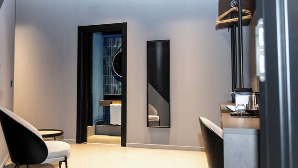 Ein modernes Hotelzimmer mit minimalistischem Design, ausgestattet mit einem großen Spiegel, einer Sitzecke und einer Küchenzeile.