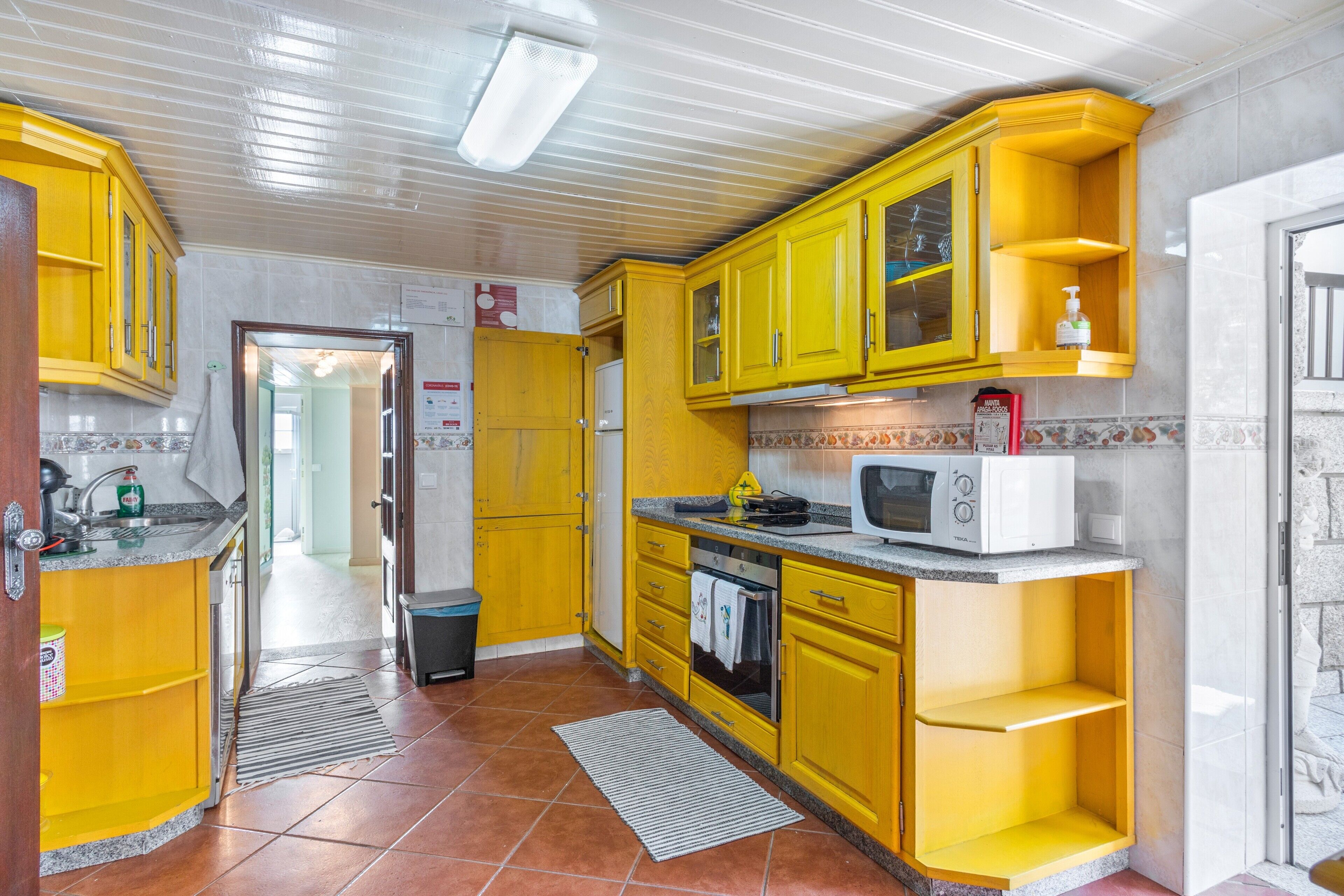 Een keuken met gele kastjes, een magnetron en een koelkast.