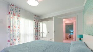 Quarto com cama, guarda-roupa, espelho e porta que dá para outro cômodo.