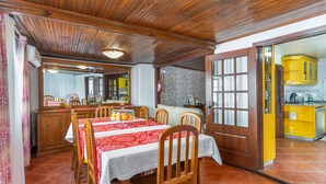 Uma sala de jantar com teto de madeira, parede de tijolos e área de cozinha amarela.