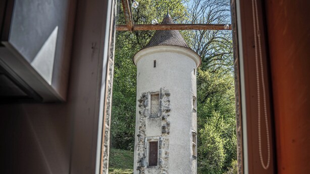 A kitchen with a window view of a white tower-like building surrounded by greenery. - Studio 2 pers en Chartreuse - balcony, village center & nature | La Borne 31 (Saint-Pierre-d'Entremont)
