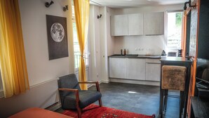 A compact room with a bed, a chair, a small table, a kitchen area, and a window with curtains. - Studio 2 pers en Chartreuse - balcony, village center & nature | La Borne 31 (Saint-Pierre-d'Entremont)
